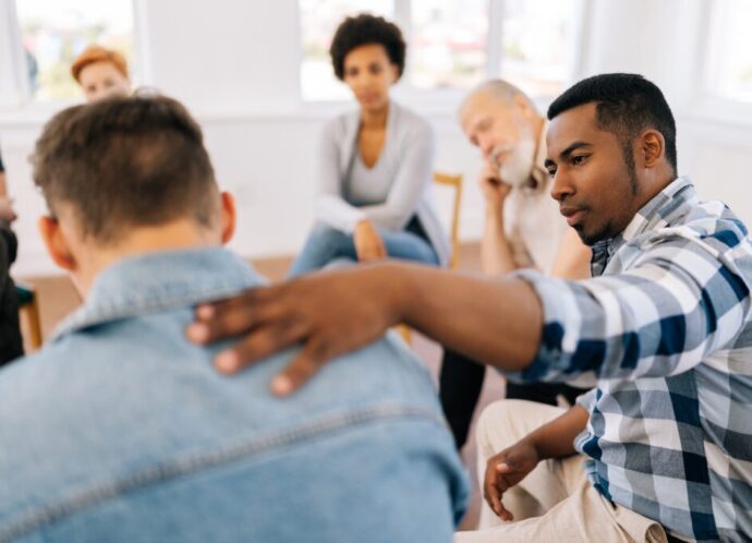 Closeup back view of unrecognizable sad man sharing life problem grief with multiracial people in modern mental health support group session in rehab center.